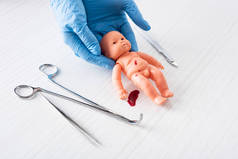 穿着蓝色乳胶手套的医生拿着婴儿娃娃，靠近医疗器械的血
