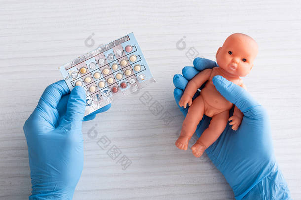 医生在乳胶手套持有堕胎药和婴儿娃娃在手中的顶视图