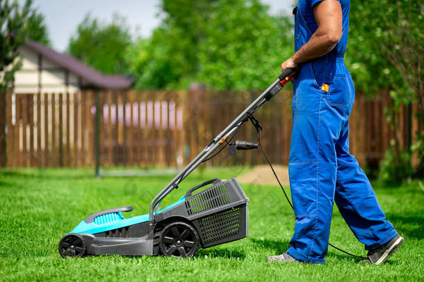 草坪割草。工人们在绿色的院子里割草.一个拿着电动割草机割草的人。园丁修剪花园