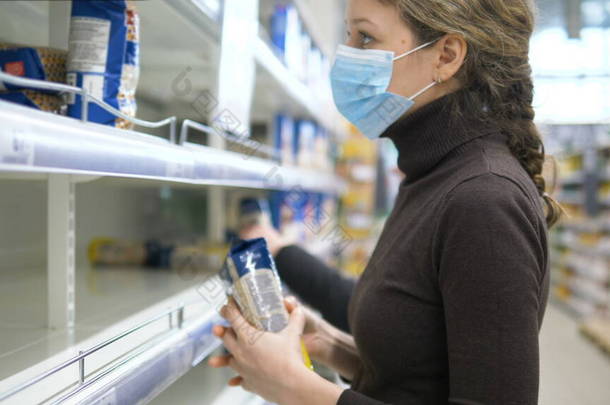 一个戴着医疗面罩的女人拿走了店里最后一袋谷物，那是空的超市货架.