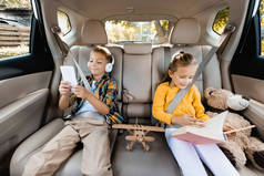 坐在车后座的玩具旁边，拿着智能手机和书笑孩子们