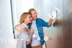 微笑的丈夫指着智能家居系统控制面板和拥抱快乐的妻子