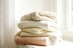 成束的针织保暖胶布色毛衣，不同的针织图案叠叠在白色窗台上，窗台背景。秋天的冬季流行针织衫.关闭，复制空间.