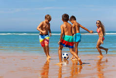 一群男孩和女孩在水边的沙滩上踢足球