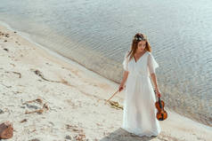 美丽的女孩在白色礼服举行小提琴在海滨