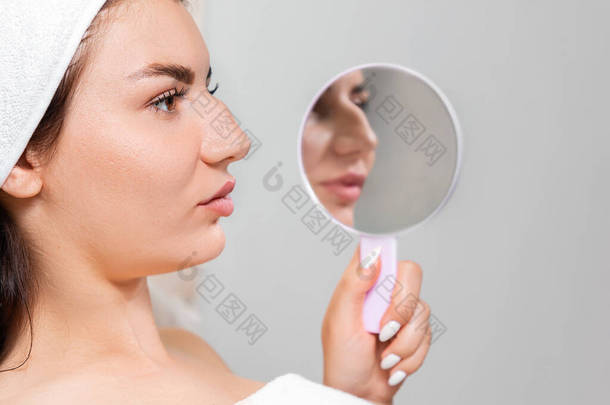 整形手术前后的对比结果.一个年轻的女人拿着一面镜子,倒映着一个驼背的鼻子.鼻成形术的概念.