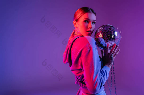 一个年轻而时髦的女人拿着闪亮的迪斯科舞会，把目光投向远方的紫色