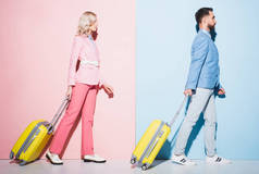 外景迷人的女人和英俊的男人背着粉色和蓝色背景的旅行包走在一起