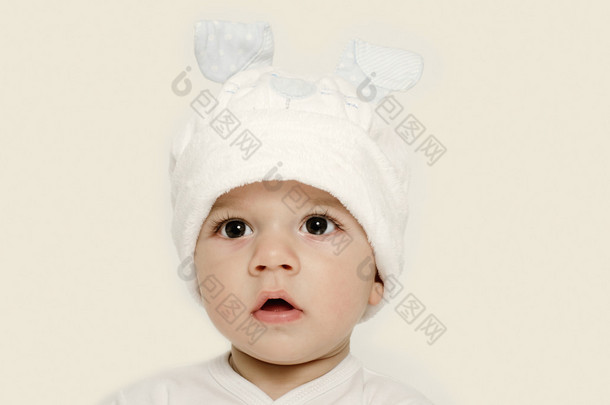 天真的孩子戴着白色的帽子，看起来很可爱。孩子穿的冬天，可爱的新生儿。可爱的宝宝画像看好奇。宝宝打扮成有趣的兔子，戴着白色帽子的兔子耳朵