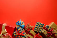 在红色纸的背景上用丝带装饰的礼品纸上的圣诞礼物的顶部视图。新年、节日和庆典装饰品的概念。复制空间。平躺