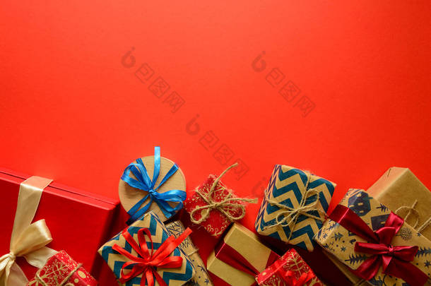 在<strong>红色</strong>纸的<strong>背景</strong>上用丝带装饰的<strong>礼品</strong>纸上的圣诞礼物的顶部视图。新年、节日和庆典装饰品的概念。复制空间。平躺