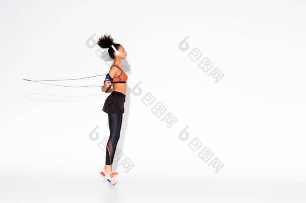 运动非洲裔美国女运动员在耳机锻炼与跳绳上白色