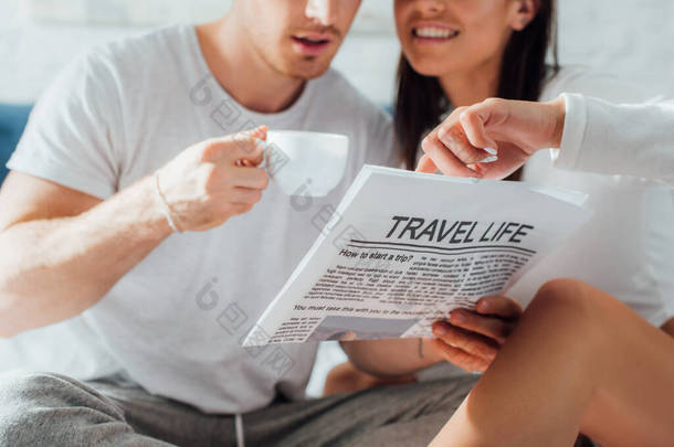 身着睡衣的年轻夫妇在家中喝咖啡、看报纸、看旅游生活文章的剪影