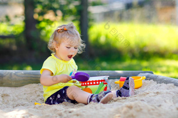 可爱的幼儿女孩在户外操场上玩沙子。美丽的婴儿在<strong>阳光</strong>明媚、温暖、<strong>阳光</strong>明媚的夏天玩得很开心.快乐健康的孩子，有<strong>沙滩</strong>玩具和五颜六色的时尚服装.