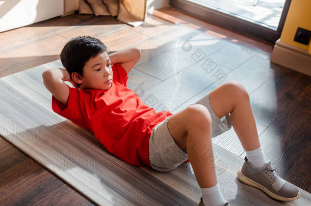 在检疫期间，亚洲男孩在家中健身垫上做腹肌运动