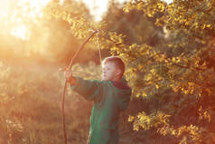 小男孩, 拍摄与手工弓和箭头在日落时的目标, 夏季户外.
