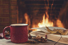 红色杯子，热茶，在燃烧的壁炉前翻开一本书，舒适，放松和温暖的炉灶概念