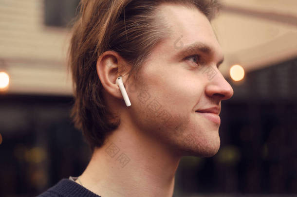 男人在户外，街上，餐馆的无线耳机。男人在听电子书，男人在听音乐。一个戴蓝牙耳机的男人正在享受生活.