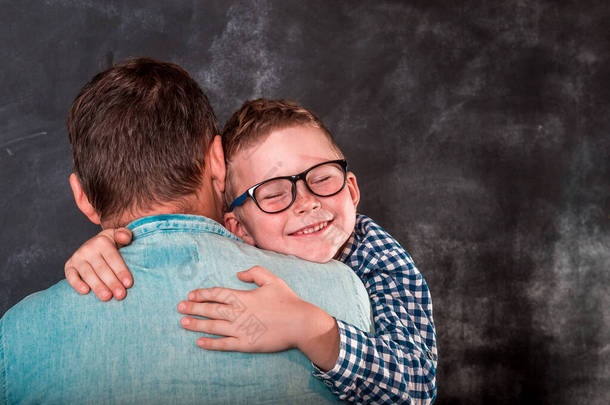 小男孩靠在她父亲的肩上.小儿子在沃尔附近拥抱他的爸爸。快乐的父亲和孩子们手头上。戴眼镜的学童。父亲节