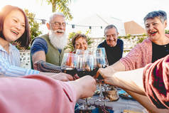 快乐的资深朋友在露台上享用红酒杯--成熟的人在户外一起用餐--老人的生活方式、饮食、退休和养老金领取者的概念