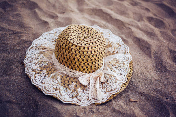 一个可爱的卡瓦花边草帽在沙滩上。深紫色色调的海滩上一顶老式礼帽的特写.