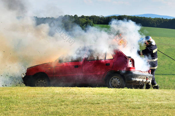 消防员扑灭了汽车上的火.红色的车着火了，烟和消防员。草地上的事故.