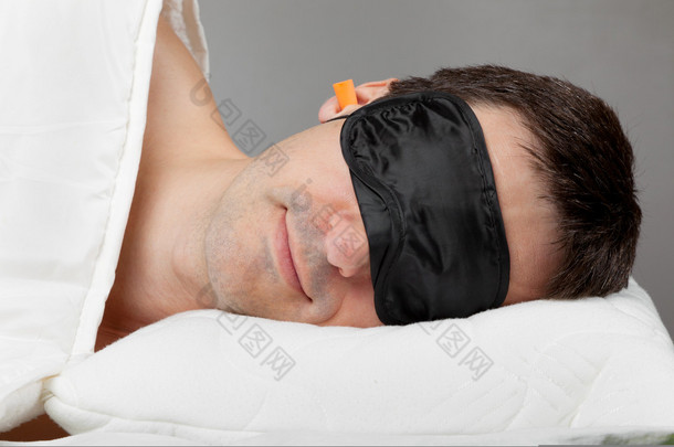 睡眠面膜睡眠和耳塞躺在床上的男人