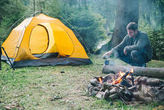 男人在金属杯里倒茶。帐篷的背景。露营概念