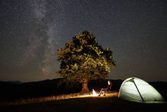 女性徒步者在夏天晚上休息在篝火附近的山上露营