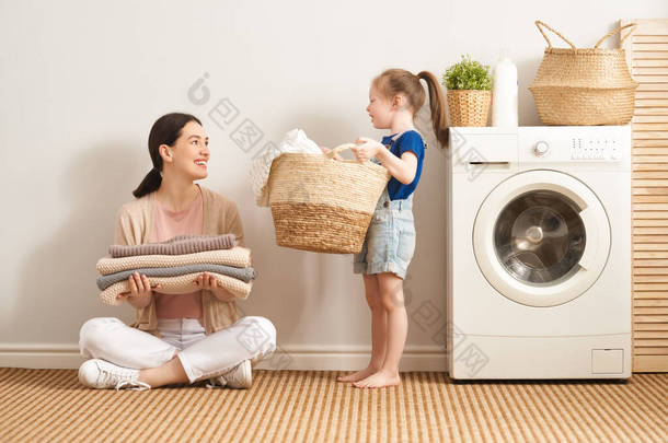 在家里洗衣服的时候，漂亮的年轻妇女和小女孩的小助手们都在开心地笑着.