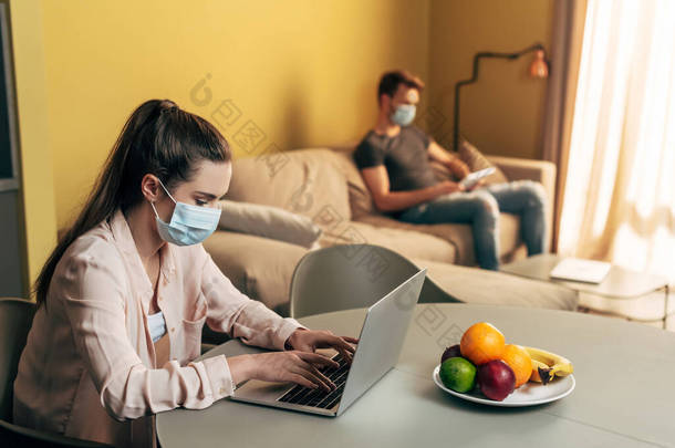 自由撰稿人在医疗面罩中的选择焦点- -在家里带数码平板电脑的人旁边用笔记本电脑