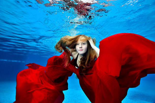 一个长着长发的可爱的小女孩的画像，她在<strong>游泳</strong>池里<strong>游泳</strong>和玩耍，手里拿着红布。时尚肖像。水下<strong>摄影</strong>。横向方向：.