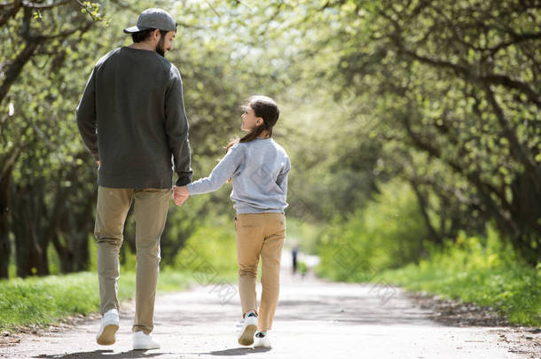 父亲和女儿的后方视图在公园里散步和牵手