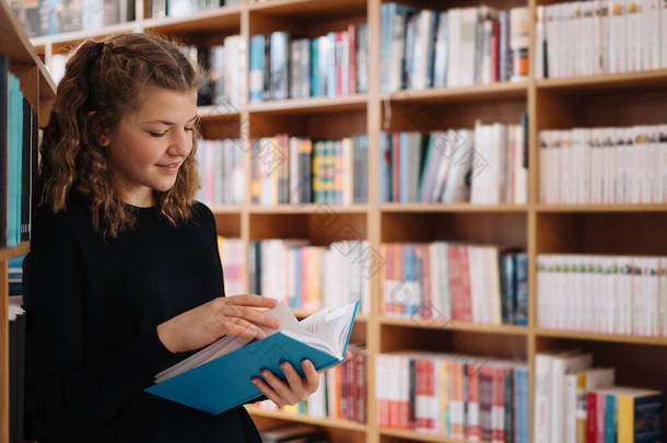 美丽的女孩站在书店的书架上看书时，正在学习看书