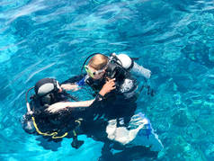两名潜水员在黑色潜水衣, 一个男人和一个女人与氧气瓶下沉在透明的蓝色水的海洋, 海洋在一个热带天堂温暖的度假胜地.