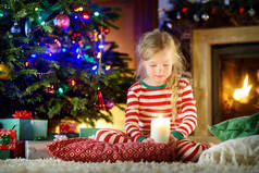 快乐的小女孩，穿着圣诞睡衣在圣诞前夜在舒适的黑暗客厅的壁炉旁玩。在家里庆祝圣诞节.