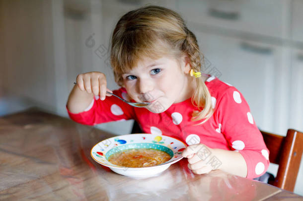 可爱的小女孩在厨房里吃新鲜的熟蔬菜汤。快乐的孩子午餐或晚餐吃健康的食物。婴儿学习。家庭、<strong>托</strong>儿所、<strong>幼儿</strong>园或日<strong>托</strong>所