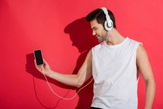 英俊的微笑的年轻男子在耳机听音乐与智能手机在粉红色