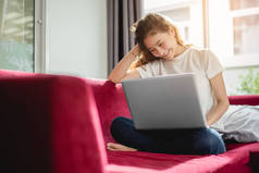 年轻妇女网上购物与互联网在愉快的心情在红色沙发。业务和工作理念, 放松和兼职概念