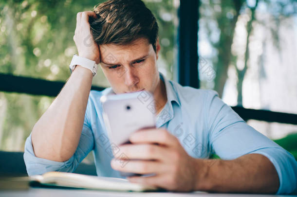沮丧的年轻人在读短信时哭着, 在现代智能手机上有坏消息。焦虑的时髦学生看视频博客上的数字电话使用4g 互联网连接