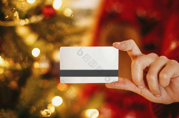美丽的年轻女子持有信用卡的背景下金色美丽的<strong>圣诞</strong>树与<strong>灯光</strong>在节日的房间。<strong>圣诞</strong>购物与销售理念