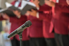 Microphone on a stand in front of mens choir members holding singing book while performing in a cath
