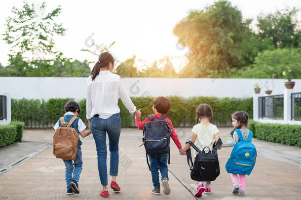 一群学龄前儿童和老师手牵手，步行回家。妈妈带她的孩子一起上学。回到<strong>学校</strong>与教育<strong>理念</strong>。人和生活方式主题。后视图