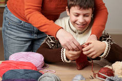 母亲正在学习她的孩子编织。木桌上有五颜六色的羊毛纱线.