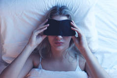 睡觉的女孩在一个与夜间照明的矫形枕头上的睡眠面具, 白色床单.