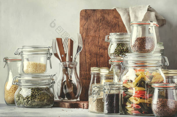 库存或一套谷物, 面食, 腹股沟, 有机豆类和有用的种子在玻璃瓶。素食主义者的蛋白质和能源资源来源。健康的素食。家庭生活场景。灰色厨房桌子背景。色调的图像
