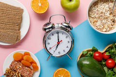 银色闹钟的顶视图与蓝色和粉红色背景的美味饮食食品