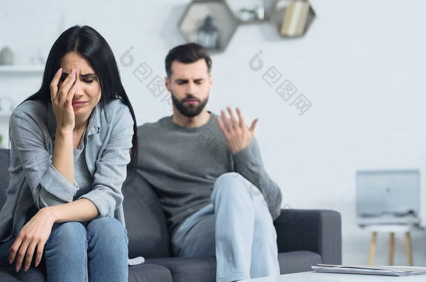 upset woman crying near blurred and displeased boyfriend quarrelling at home