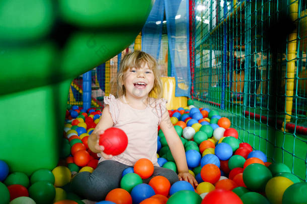 活泼的小女孩在室内操场上玩耍。快乐快乐的学龄前儿童攀爬，奔跑，跳跃，并有乐趣与五彩缤纷的塑料球。儿童的室内活动.