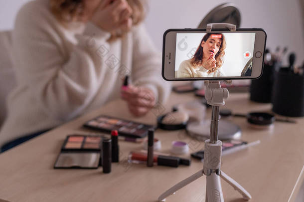 年轻的高加索女人正在她的手机上记录一个在线化妆训练视频。视频博客女孩化妆.